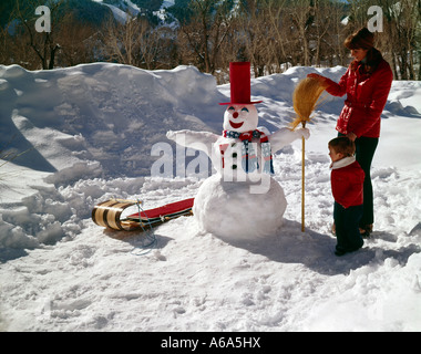 Giovane madre e figlio di costruire un pupazzo di neve in una giornata invernale Foto Stock