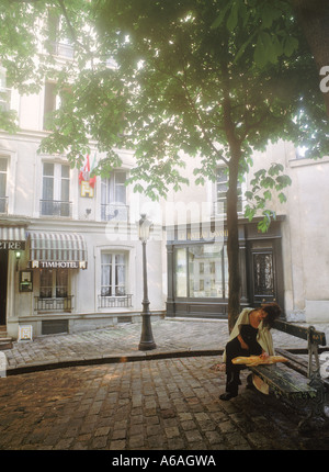 Donna parigina con baguette in appoggio sul banco in una tranquilla piazza di Montmartre Foto Stock