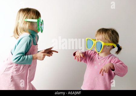 Due ragazze messing about con grande scherzo occhiali da sole sui bicchieri bambini divertirsi attraverso il gioco Foto Stock