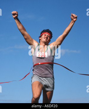 Runner maschio rompere il nastro al traguardo di una corsa podistica Foto Stock