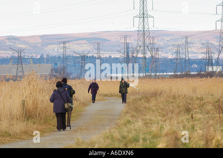 Walkers sul sentiero con tralicci in distanza a Newport Zone Umide Riserva Naturale Nazionale South East Wales UK Foto Stock