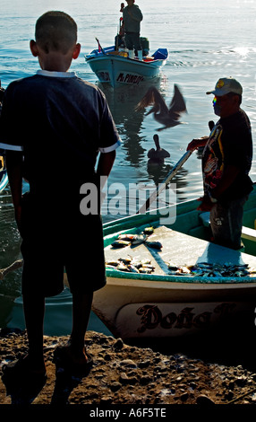 Ragazzo a guardare le barche dei pescatori venire a. Nessun modello di rilascio non Viste posteriore e hi contrasto ombra significa che le persone non sono riconoscibili Foto Stock