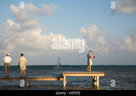 BELIZE Ambergris Caye tre maschi adulti pratica la pesca con la mosca colata dal dock in legno e la piattaforma windsurf nei Caraibi Foto Stock