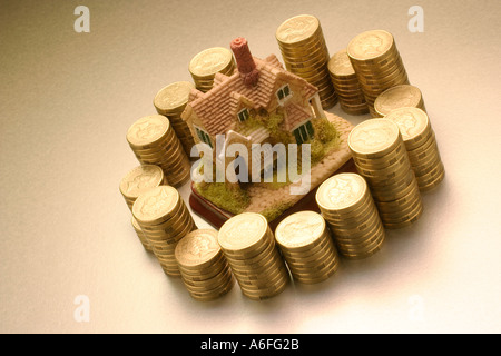 Casa figurina circondato da pile di monete Foto Stock