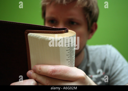 Bionda e giovane uomo leggendo la Bibbia con un luminoso sfondo verde Foto Stock