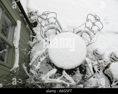 Neve sul ferro francese di tavolo e sedie da giardino accanto a un tongued e scanalati portico verde Foto Stock