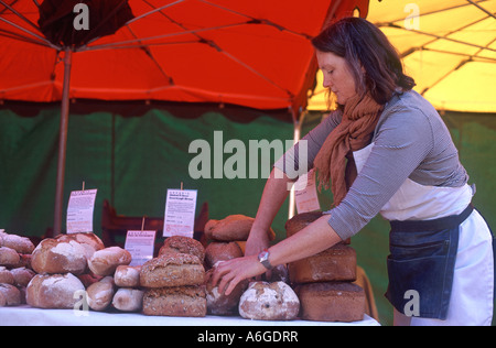 Donna disponendo le pagnotte di pane organico sotto il rosso e il giallo di ombrelli del suo stallo a Borough Market, Southwark, Londra Foto Stock