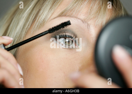 Giovane donna cercando in un handmirror applicazione di mascara con un pennello. Foto Stock