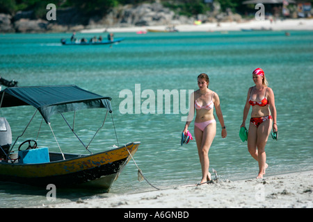 Due giovani donne in bikini a piedi passato ancorato barca lunga spiaggia Perhentian Kecil Malaysia Foto Stock