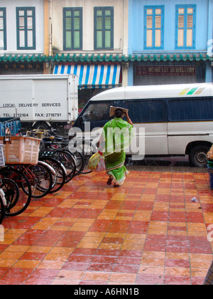 Donna in sari con protezioni shopping capelli dalla pioggia con il giornale di Little India di Singapore Foto Stock