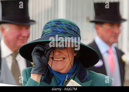 Donna al Royal Ascot cavallo di razza, guardando attraverso il binocolo, York, Gran Bretagna Foto Stock