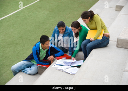Gruppo multirazziale di quattro adolescenti studenti senior seduta rilassante e studiare insieme sui passi dalla scuola sportsfield Foto Stock