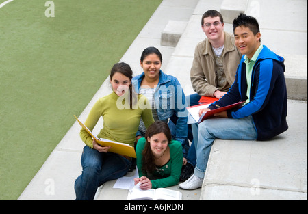 Gruppo multirazziale di cinque adolescenti studenti senior di sedersi e rilassarsi insieme sui passi dalla scuola campo sportivo Foto Stock