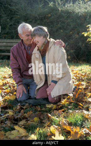 Felice Coppia matura inginocchiato tra foglie di autunno Foto Stock
