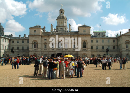 Turisti per la sfilata delle Guardie a Cavallo guarda la modifica della cerimonia di guard tour guida e ombrello giallo & gruppo di persone Westminster Londra Inghilterra REGNO UNITO Foto Stock