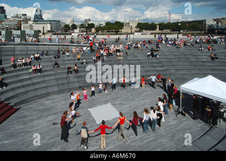 Gli spettatori in occasione di Musica & Danza evento presso il convogliatore riverside anfiteatro bambini tenendo le mani in un cerchio City di Londra e Torre di Londra al di là di Regno Unito Foto Stock