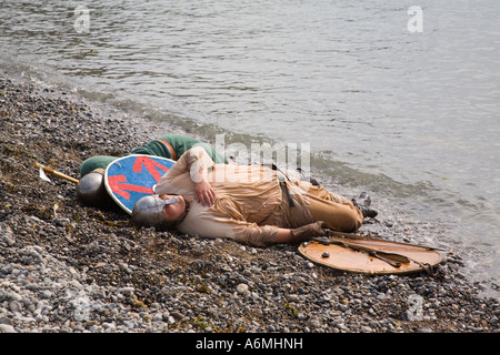 AMLWCH BIENNALE FESTIVAL VIKING Viking attore con scudo playing dead a bordo di acqua sulla spiaggia dopo la battaglia di re promulgazione Foto Stock