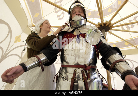 Combattere vecchie battaglie. Una servetta maliziosa abito aiuta un coraggioso cavaliere nella sua corazza come parte di un torneo medievale. Foto Stock