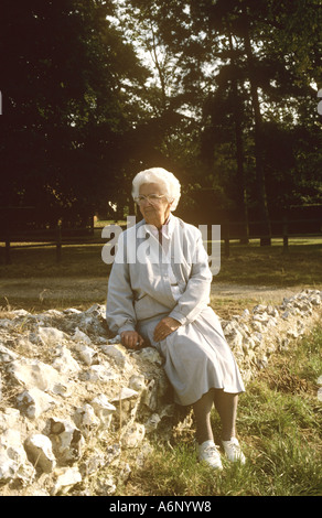 Donna anziana seduta sulla parete Foto Stock