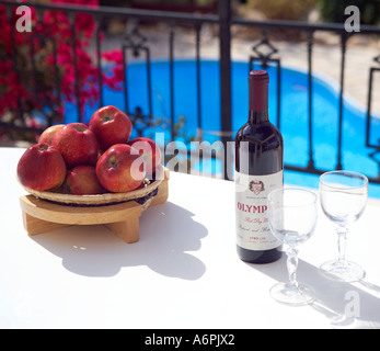 Un tavolino a bordo piscina impostazione con una bottiglia di vino rosso locale e i bicchieri per due con una coppa di frutta Foto Stock