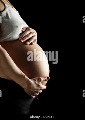 Donna incinta tenendo la pancia ritagliata su sfondo nero Foto Stock