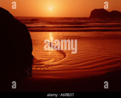 Receding maree creare un pattern al tramonto nella sabbia di una spiaggia di Oregon Foto Stock