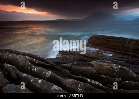 Il sole tramonta dietro le nuvole a Elgol sull'Isola di Skye, lasciando un dark scena costiere solo con macchie di colore Foto Stock