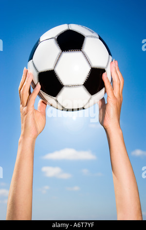 Donna di mani tenendo palla calcio sotto il cielo blu Foto Stock