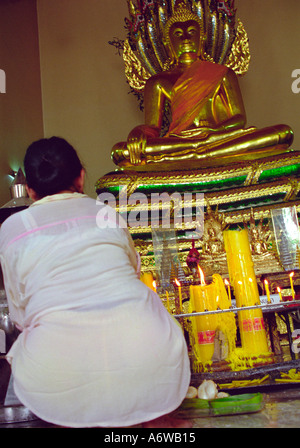 Donna accendendo candele davanti a un Buddha d'oro di Bangkok in Thailandia Foto Stock