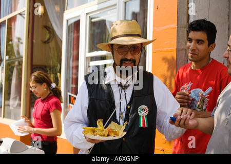 ILLINOIS Chicago Uomo nel cappello di paglia portano piatto di cibo il marciapiede nel quartiere Pilsen di giovani adulti Foto Stock