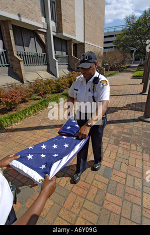 Femmina nero di funzionari di polizia prendere l'America bandiera verso il basso una piega che alla fine della giornata a Montgomery in Alabama al Foto Stock