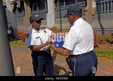 Femmina nero di funzionari di polizia prendere l'America bandiera verso il basso una piega che alla fine della giornata a Montgomery in Alabama al Foto Stock