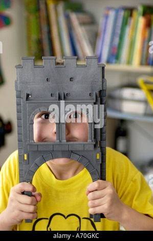 Funny sette anno vecchio ragazzo cerca attraverso il cancello del suo giocattolo cavaliere del castello Foto Stock