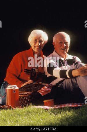 Coppia senior seduta sul prato avente un picnic Foto Stock