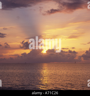 Tramonto sul mare calmo con dolci increspature grigio nuvole drammatico sull orizzonte raggi solari in sky west coast Antigua nei Caraibi Foto Stock