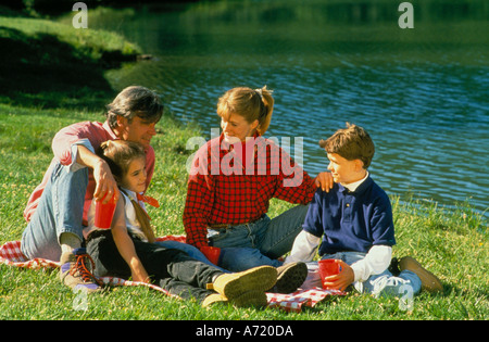 La famiglia del padre di una Figlia di madre e figlio avente un picnic seduti su una coperta in prossimità di un lago Foto Stock