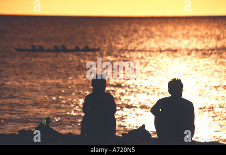 Dragon Boat in acqua frizzante con persone che guardano dalla spiaggia nella luce del tramonto Oahu Hawaii Foto Stock