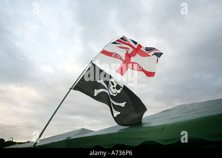 Tre bandiere che sventolano al di sopra di una tenda contro un cielo scuro, il Jolly Roger (Teschio e Ossa Croce) Saint Georges, e l'Unione Jack Foto Stock