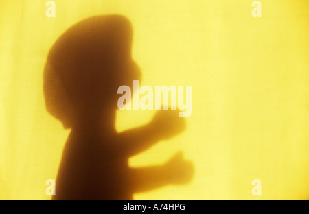 Ombra nella luce calda sul panno pallido o tenda della tradizionale baby doll in piedi o prendendo timidi passi verso la luce Foto Stock