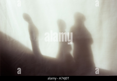 Ombra nella luce calda sul panno pallido o tenda del modello di tre figure raggruppate con una standing distanti come se respinta o disonore Foto Stock