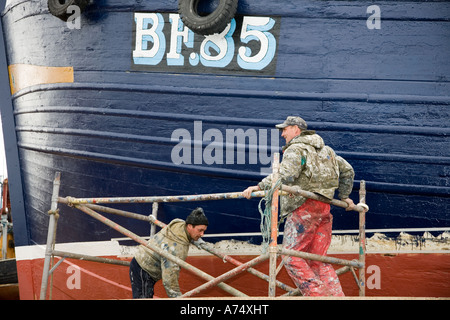 Operai pittura barca nave numero. Un pittore di navi a MacDuff navi e barche da pesca cantiere di riparazione a nord-est della Scozia uk Foto Stock