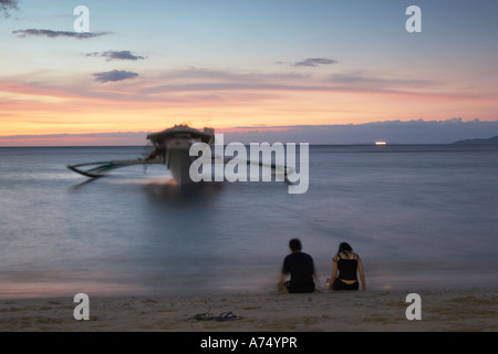 Giovane seduto sulla spiaggia al tramonto Foto Stock