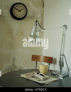 Close-up di classic Anglepoise cromo lampada sul tavolo con cup e i notebook in semplice sala da pranzo con il vecchio orologio circolare sulla parete Foto Stock