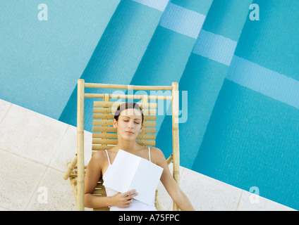 Donna che Dorme in poltrona a bordo della piscina con un libro sul petto Foto Stock