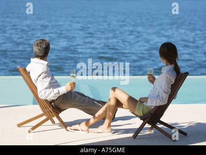 Giovane seduto con bicchieri di champagne, con vista sul mare Foto Stock