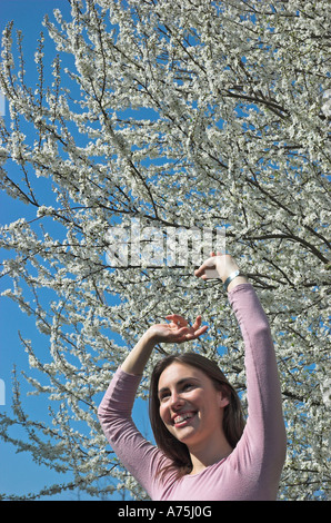 Giovane donna bracci di estensione sotto la molla blossom tree Foto Stock