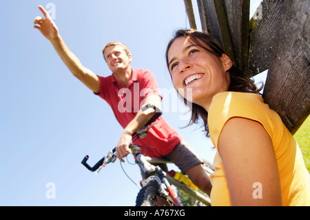 Uomo seduto sulla bicicletta, donna appoggiata sulla ringhiera in legno, sorridendo a basso angolo di visione Foto Stock