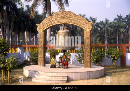 Tre ragazzi tibetano pongono sotto la grande Campana in ottone con ornato cornice al Vihara Mulagandhakuti nel parco dei cervi Sarnath India Foto Stock