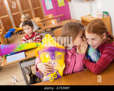 Le ragazze (4-7) tenendo cono scuola whispering in aula, vista di inclinazione Foto Stock