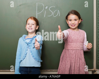 Le ragazze (4-7) in piedi dalla lavagna, mostrando pollice in alto segno Foto Stock